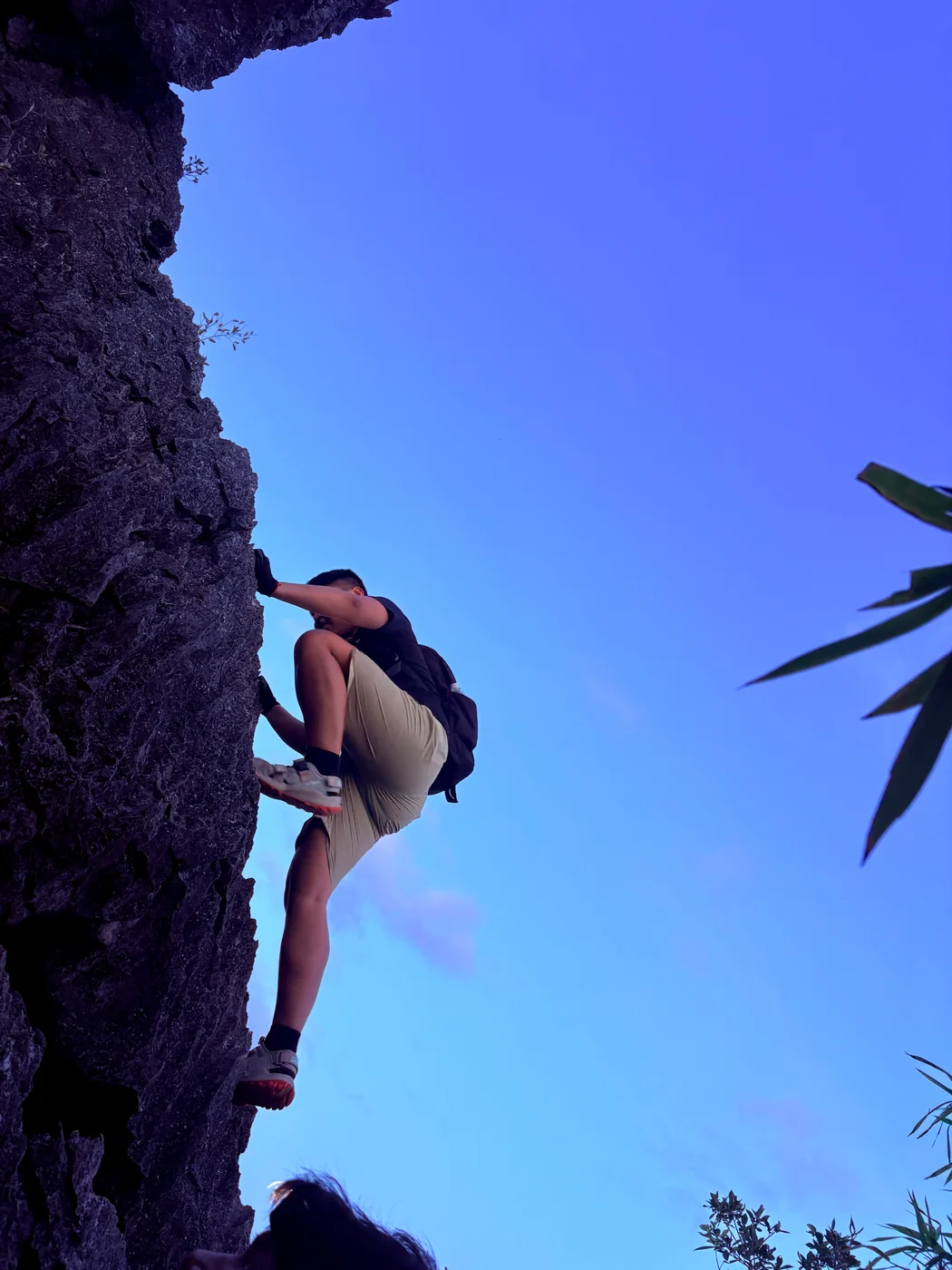 Alex climbing an outdoor rock face beneath a blue sky