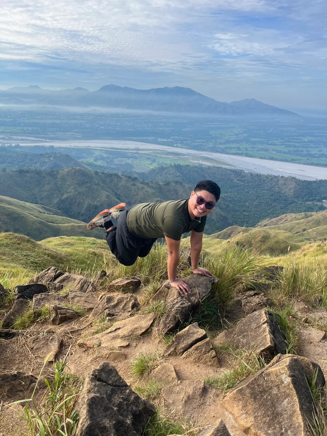 Alex on a grassy mountain summit with a wide valley behind him