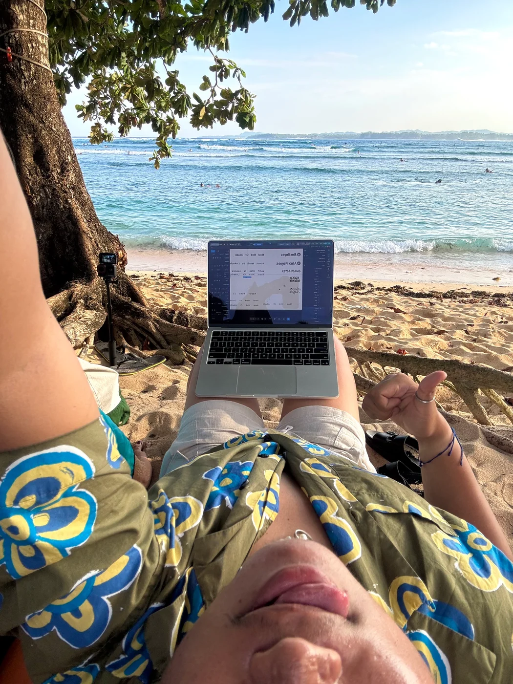 Relaxing beneath a tree with a laptop beside the beach